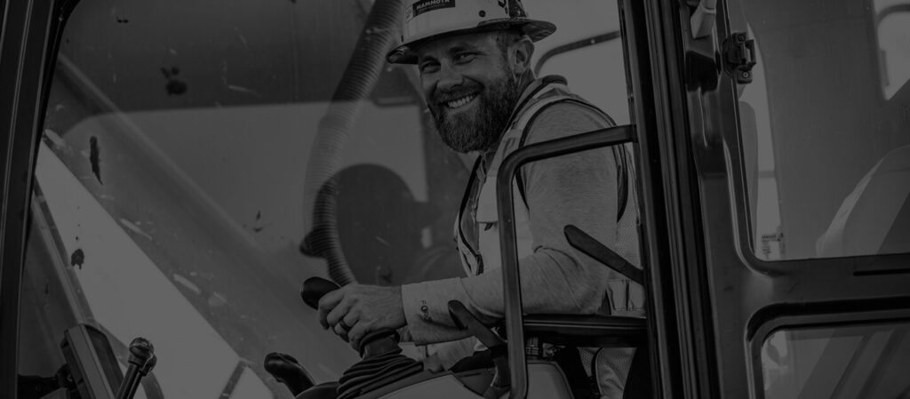 Construction worker smiling from the window of a construction vehicle.