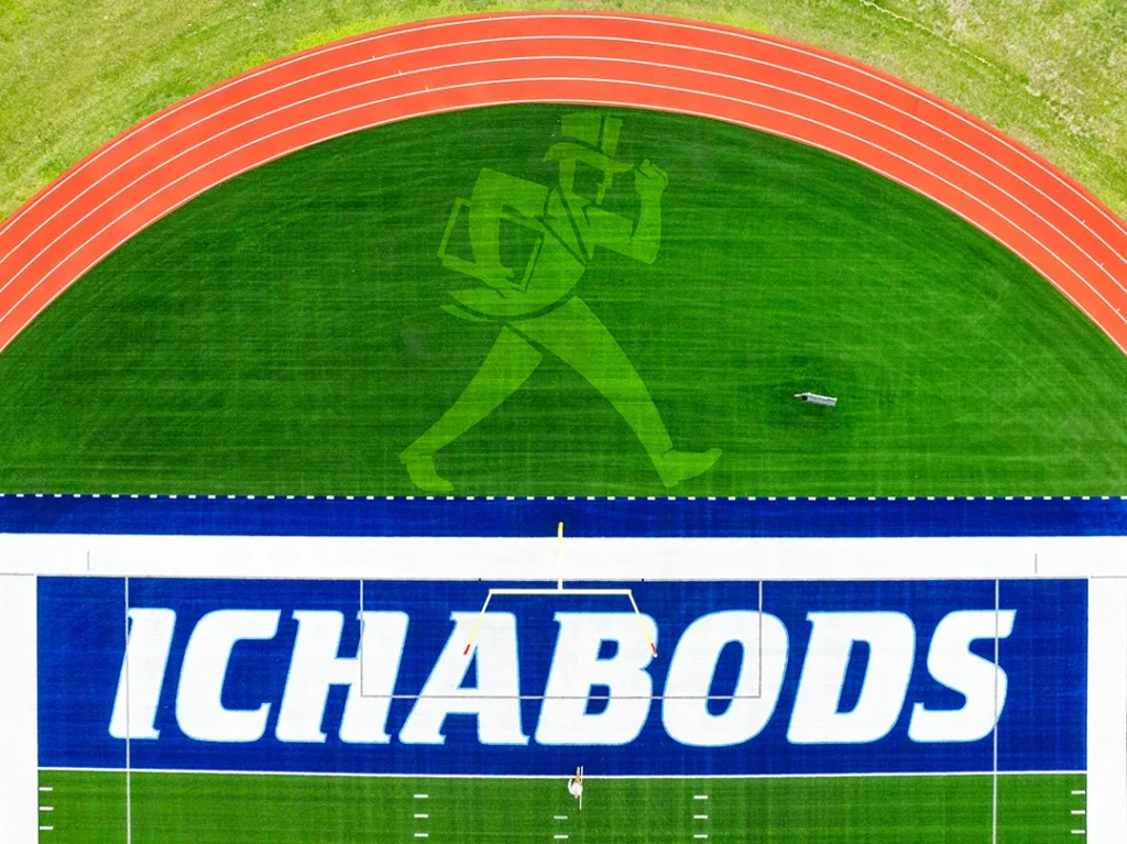 Washburn's navy end zone with ICHABODS in bold white letters outlined in baby blue, above a tone-on-tone Ichabod mascot woven into the green turf