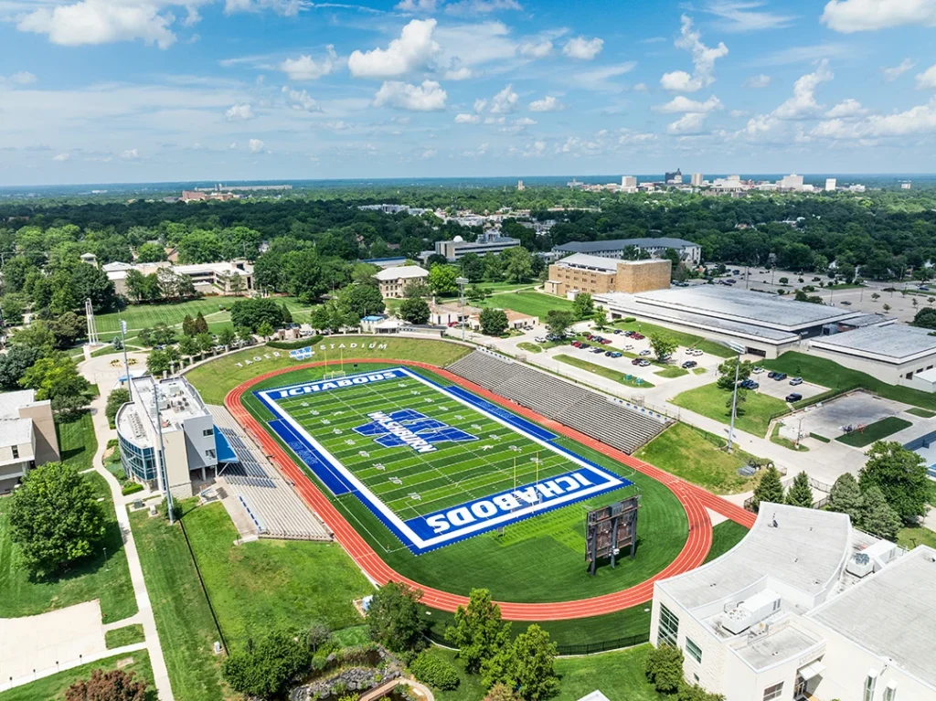 Wide aerial of the Washburn University campus in Topeka with Yager Stadium and its ICHABODS field in the foreground under a blue sky