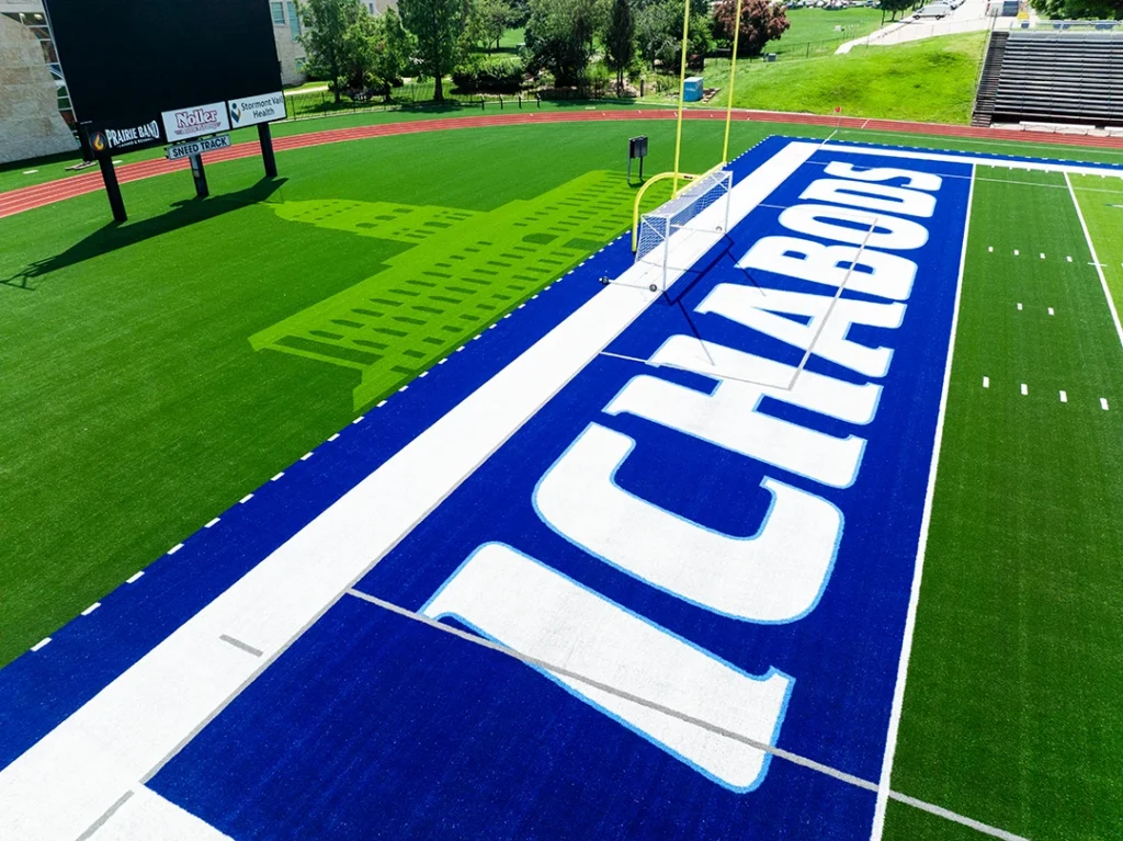 Low-angle drone view of the ICHABODS lettering in Washburn's navy blue end zone, with the stadium scoreboard and stands in the background