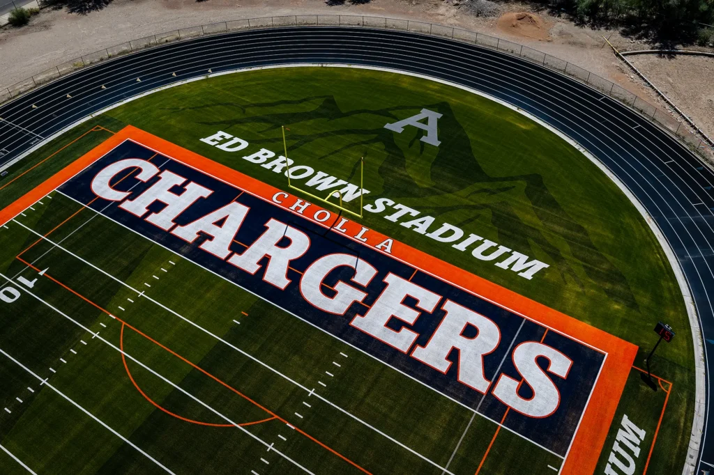 Close aerial view of the Cholla Chargers end zone, with “ED BROWN STADIUM” lettering and a mountain graphic inlaid in the turf.