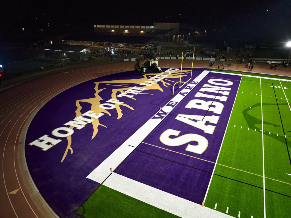 Close aerial view of the Sabino Sabercats end zone, with “Home of the Sabercats” lettering and a mountain graphic inlaid in the turf.